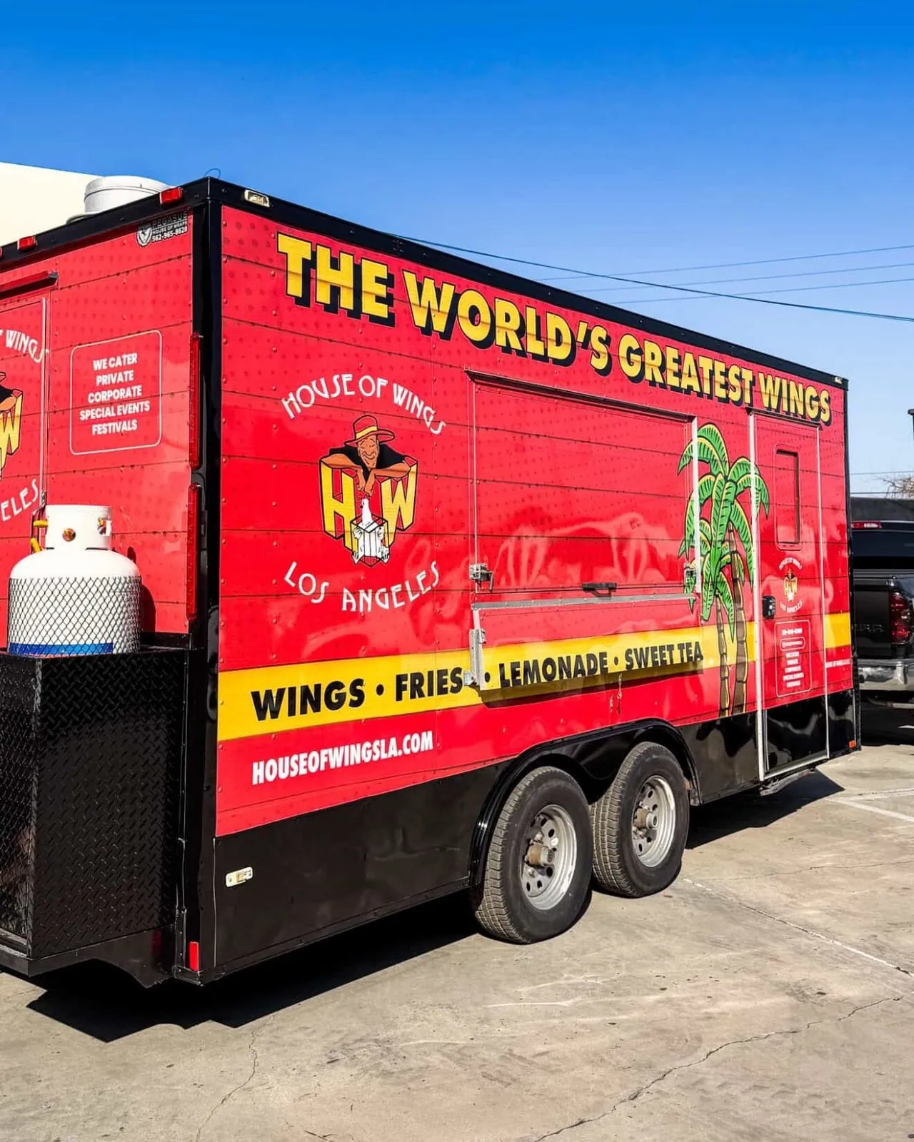 The finished trailer on a Los Angeles lot, three quarter view. High contrast red and yellow wrap with the House of Wings mark, built to be read from down the block.
